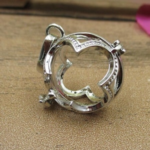 May include: A silver-toned metal charm with a delicate, openwork design resembling a butterfly. The charm is round and has a hinged opening.