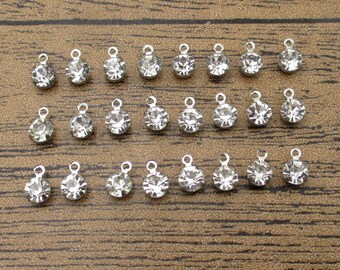 May include: A collection of 25 silver-toned charms with clear crystal rhinestones. Each charm features a loop for attaching to jewelry or other crafts.