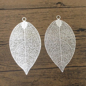 May include: Two silver leaf-shaped metal charms with a delicate, intricate design. The charms have a hole at the top for attaching to jewellery or other crafts.