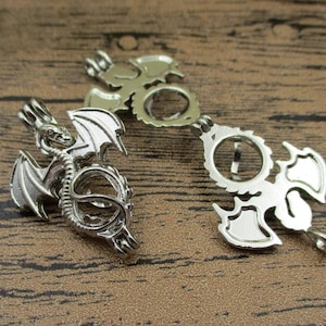 Op de afbeelding: Twee zilveren drakenhanger. Een hanger is open en de andere is gesloten. Beide hangers hebben een gedetailleerd drakenontwerp.