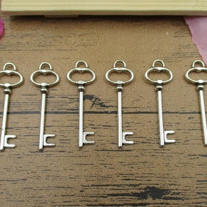 May include: Seven silver-toned skeleton keys with ornate keyholes and a simple design. The keys are arranged in a row on a wooden surface.