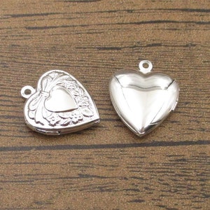 May include: Two silver heart-shaped locket pendants. One locket has a detailed design with a heart in the center, while the other is plain.
