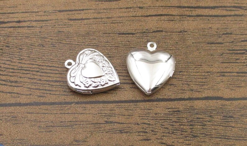May include: Two silver heart-shaped locket pendants. One locket has a detailed design with a heart in the center, while the other is plain.
