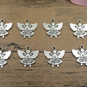 Puede incluir: Ocho encantos de ángel de plata con alas y el texto "Angels watch over me" y un pequeño corazón.