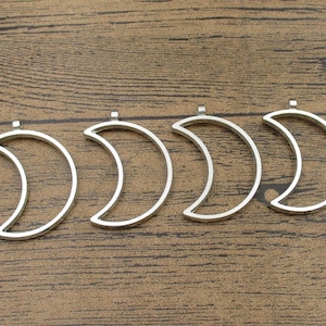 Peut inclure: Quatre breloques en métal en forme de croissant de lune argentées avec une boucle en haut pour les attacher à des bijoux ou d'autres objets artisanaux.