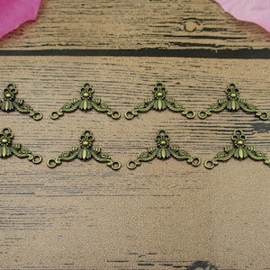 May include: Eight antique gold-toned metal connector charms with a floral design. Each charm has three loops for attaching to other jewellery pieces.