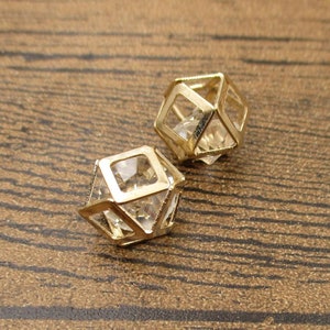 Puede incluir: Dos pendientes geom&eacute;tricos de tono dorado con detalles de cristal transparente. Los pendientes tienen forma de cubos con los lados abiertos.