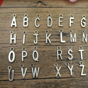 May include: Silver alphabet letter charms with a loop for hanging. The letters are arranged in alphabetical order from A to Z.