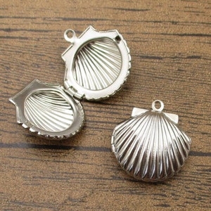 Könnte beinhalten: Drei silberfarbene Anhänger in Muschelform. Die Anhänger sind offen und haben ein detailliertes, geripptes Design.