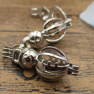 Op de afbeelding: Drie zilveren bedelkooien met ingewikkelde ontwerpen. De kooien zijn open en hebben een delicate, sierlijke uitstraling.