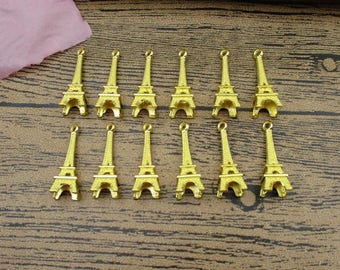 May include: A set of 12 gold-coloured Eiffel Tower charms. The charms are approximately 5 cm tall and have a loop at the top for attaching to jewellery or other crafts.