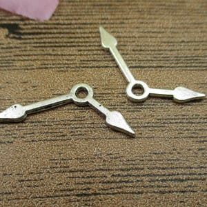 May include: Two silver-toned clock hands with pointed ends. The hands are bent at a 90-degree angle.