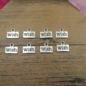 May include: Eight silver charm tags with the word "wish" engraved on each. The tags are arranged in two rows of four on a wooden surface.