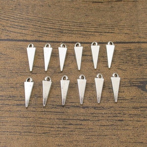 May include: A set of 12 silver triangle charms with a loop at the top. The charms are arranged in two rows of six on a wooden surface.