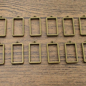 以下が含まれることがあります： 上部に吊り下げ用のループが付いた、アンティークゴールド調の金属製の長方形フレームが12個。フレームは2列6個ずつ配置されています。