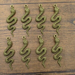 May include: Ten antique gold-toned snake charms. Each charm features a detailed snake design with a textured surface. The charms are perfect for jewellery making or crafting projects.