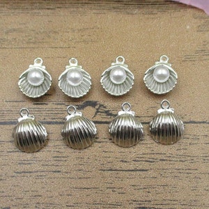 May include: Ten silver-toned metal charms shaped like seashells. Five of the charms have a white pearl in the center.