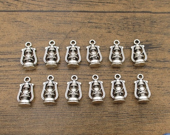 May include: A set of 12 silver-toned metal charms shaped like antique oil lamps. The charms are approximately 1 inch in length and have a loop at the top for attaching to jewelry or other crafts.