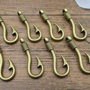 May include: Ten antique gold-toned metal fishing hook charms. The hooks are approximately 5 cm long and have a detailed design.