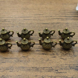 May include: Eight small, antique gold-toned teapot charms. The teapots have a detailed design and are perfect for adding a touch of vintage charm to jewelry or crafts.