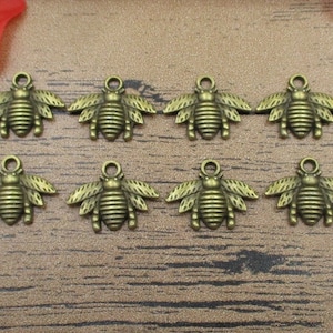 May include: Eight antique gold bee charms with wings and a textured body. The charms have a loop at the top for attaching to jewelry or other crafts.
