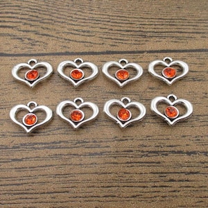 May include: Ten silver heart-shaped charms with orange rhinestone accents.