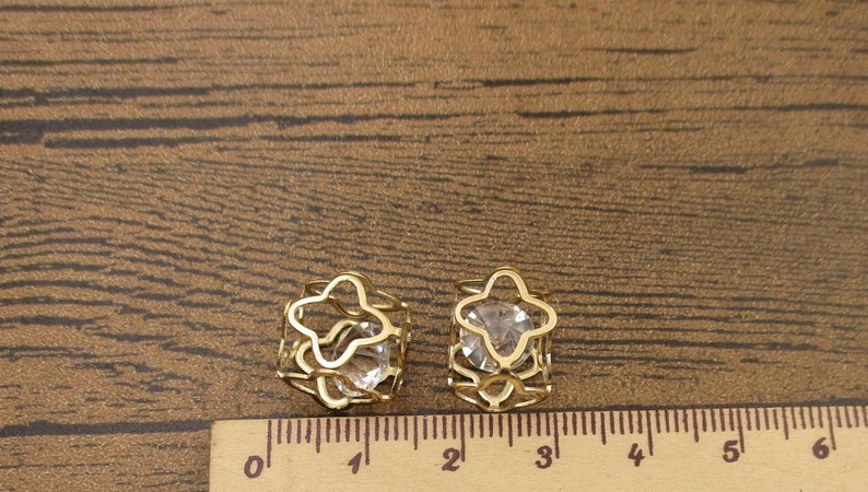 May include: Two gold-tone hair clips with clear crystal stones in the center. The clips are shaped like a star and are about 1 inch in diameter.