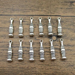 May include: A set of 12 silver-toned bottle charm pendants. Each charm is shaped like a soda bottle with a detailed design. The charms are perfect for adding a vintage touch to jewelry or crafts.
