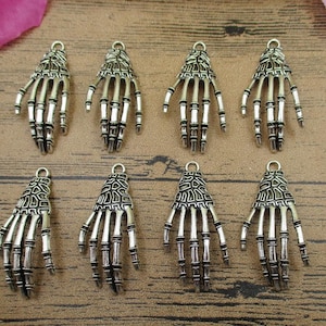 May include: Eight silver skeleton hand charms with a detailed bone design. Each charm has a loop at the top for attaching to jewelry or other crafts.