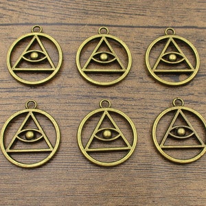 Puede incluir: Seis dijes de metal dorado con un ojo que todo lo ve dentro de un triángulo. Los dijes son de forma circular y tienen un bucle en la parte superior para sujetarlos a un collar o pulsera.