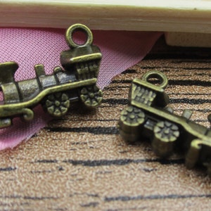 May include: Two antique gold-toned metal train charms. The charms are detailed with wheels, windows, and a smokestack. The charms are perfect for adding a vintage touch to jewelry or crafts.