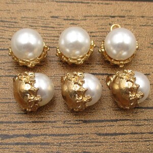 Puede incluir: Seis botones de perla blanca con engastes de metal dorado. Los botones tienen un dise&ntilde;o decorativo y ornamentado.