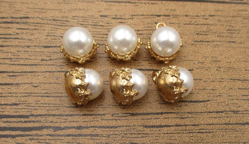Puede incluir: Seis botones de perla blanca con engastes de metal dorado. Los botones tienen un dise&ntilde;o decorativo y ornamentado.