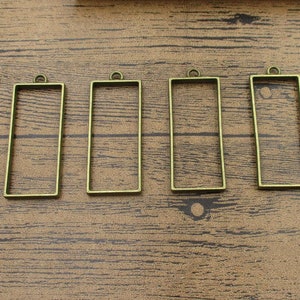 Puede incluir: Cuatro marcos rectangulares de metal de color dorado antiguo con un bucle en la parte superior para colgar. Los marcos están vacíos y listos para resina u otros proyectos de artesanía.