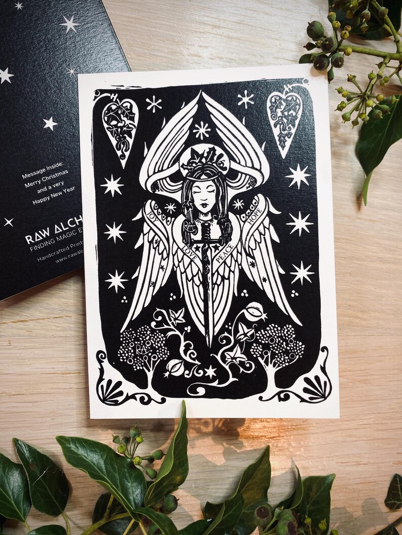 K&ouml;nnte beinhalten: Schwarz-Wei&szlig;-Kunstdruck eines Engels mit ausgebreiteten Fl&uuml;geln und einem Schwert. Der Druck enth&auml;lt die Worte "LOVE", "PEACE" und "HOPE". Die Karte tr&auml;gt auch den Text "Merry Christmas and a very Happy New Year".