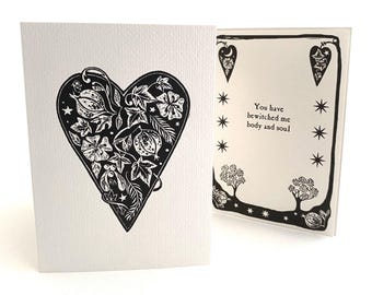 Könnte beinhalten: Eine weiße Grußkarte mit einer schwarzen Herzillustration, die mit botanischen Motiven wie Blättern und Blumen gefüllt ist. Das Innere der Karte zeigt den Text, You have bewitched me body and soul, umrahmt von Sternen, Bäumen und herzförmigen Symbolen.