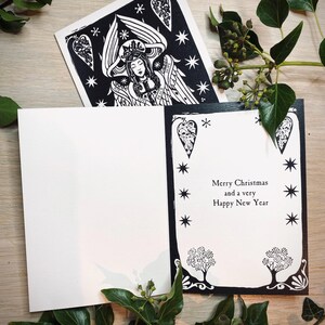 K&ouml;nnte beinhalten: Schwarz-wei&szlig;e Weihnachtskarte mit Engel-Illustration und dem Text "Merry Christmas and a very Happy New Year". Die Karte ist von gr&uuml;nen Bl&auml;ttern umgeben.