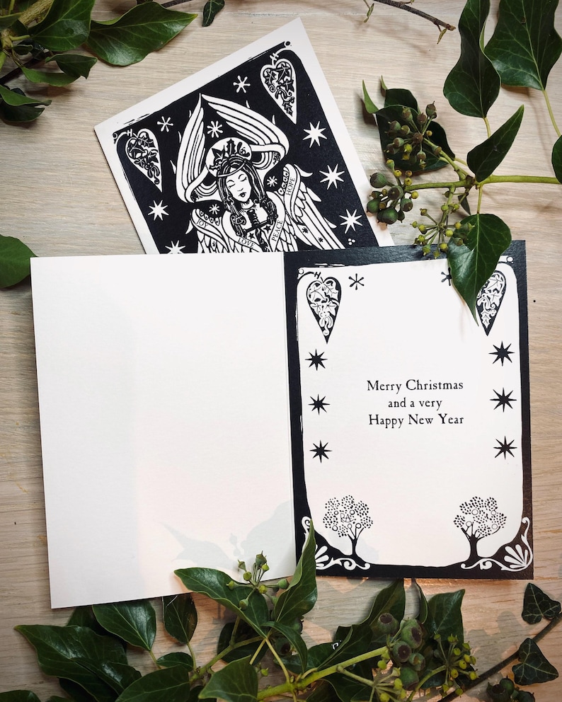 K&ouml;nnte beinhalten: Schwarz-wei&szlig;e Weihnachtskarte mit Engel-Illustration und dem Text "Merry Christmas and a very Happy New Year". Die Karte ist von gr&uuml;nen Bl&auml;ttern umgeben.