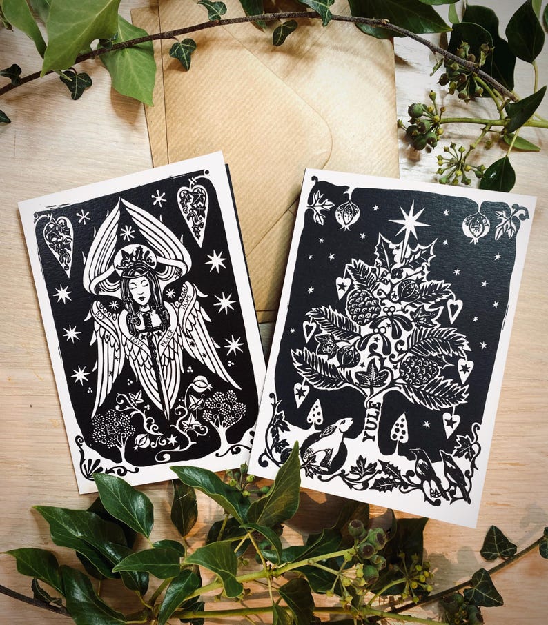 K&ouml;nnte beinhalten: Zwei schwarz-wei&szlig;e Kunstkarten mit detaillierten Illustrationen. Eine zeigt einen Engel, die andere einen stilisierten Baum mit einem Stern. Die Karten haben wei&szlig;e R&auml;nder und liegen auf einer Holzoberfl&auml;che mit Bl&auml;ttern und einem braunen Umschlag.