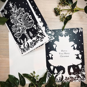K&ouml;nnte beinhalten: Schwarz-wei&szlig;e Weihnachtskarten mit einem Baumdesign, mit dem Text "Have a Very Merry Christmas". Die Karten haben eine detaillierte Illustration eines Baumes mit Sternen, Beeren und Waldtieren. Gr&uuml;ne Bl&auml;tter und Beeren umgeben die Karten.