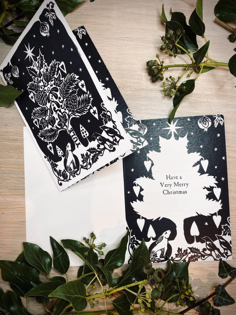 K&ouml;nnte beinhalten: Schwarz-wei&szlig;e Weihnachtskarten mit einem Baumdesign, mit dem Text "Have a Very Merry Christmas". Die Karten haben eine detaillierte Illustration eines Baumes mit Sternen, Beeren und Waldtieren. Gr&uuml;ne Bl&auml;tter und Beeren umgeben die Karten.
