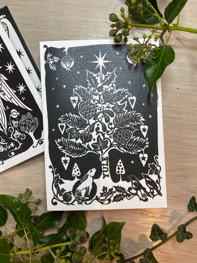 K&ouml;nnte beinhalten: Schwarz-wei&szlig;e Yule-Gru&szlig;karte mit einem stilisierten Weihnachtsbaum-Design. Der Baum ist mit Sternen, Herzen und anderen festlichen Elementen geschm&uuml;ckt. Ein Hase und V&ouml;gel befinden sich am Fu&szlig;e des Baumes. Das Wort "YULE" ist vertikal gedruckt.