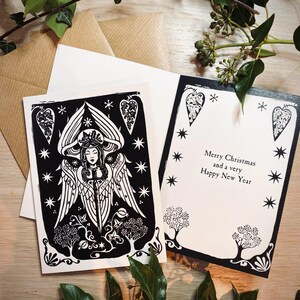 K&ouml;nnte beinhalten: Schwarz-Wei&szlig;-Weihnachtskarten mit Engel- und Sterndesigns. Eine Karte zeigt eine Engel-Illustration, die andere lautet "Merry Christmas and a very Happy New Year". Inklusive brauner und wei&szlig;er Umschl&auml;ge.