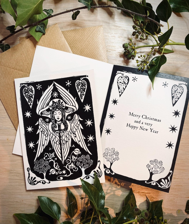 K&ouml;nnte beinhalten: Schwarz-Wei&szlig;-Weihnachtskarten mit Engel- und Sterndesigns. Eine Karte zeigt eine Engel-Illustration, die andere lautet "Merry Christmas and a very Happy New Year". Inklusive brauner und wei&szlig;er Umschl&auml;ge.