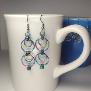 May include: A pair of iridescent rainbow earrings with multiple interlocking circles. The earrings are made of metal and have a hook closure.