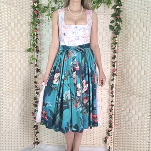 May include: A sleeveless dress with a square neckline and a floral print skirt. The bodice is light pink with a pattern, and the skirt is teal with large flowers. The dress is paired with pink heels.