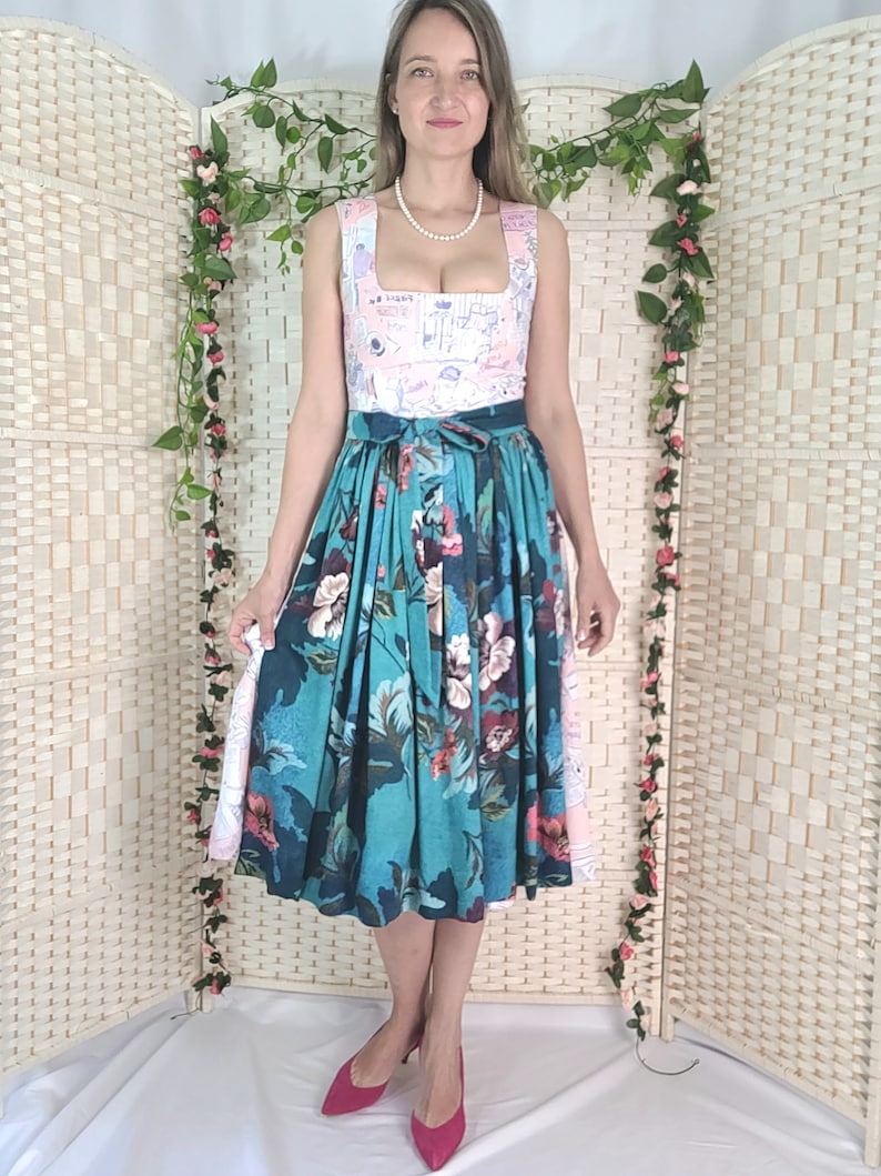 May include: A sleeveless dress with a square neckline and a floral print skirt. The bodice is light pink with a pattern, and the skirt is teal with large flowers. The dress is paired with pink heels.