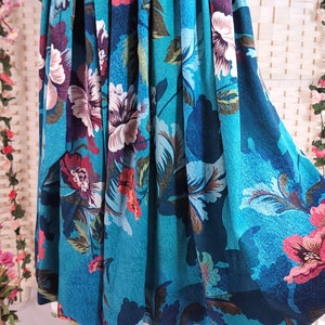 May include: A teal skirt with a floral pattern featuring large pink, white, and purple flowers. The skirt has a wide waistband with a matching tie and is displayed on a white dress form. The fabric has a corduroy texture.