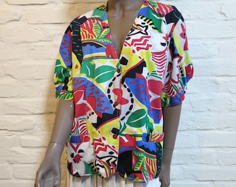 Könnte beinhalten: Eine farbenfrohe Vintage-Bluse mit Knöpfen und V-Ausschnitt. Die Bluse hat ein lebendiges abstraktes Muster mit roten, blauen, gelben, grünen und schwarzen Formen. Das kurzärmelige Oberteil wird mit einem weißen Rock kombiniert. Die Bluse hat zwei Taschen.