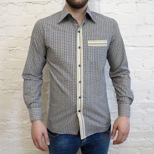 May include: A long-sleeve button-down shirt with a geometric pattern in navy blue and gold. The shirt features a contrasting stripe down the front and on the pocket, with blue buttons. The cuffs also have a geometric pattern.